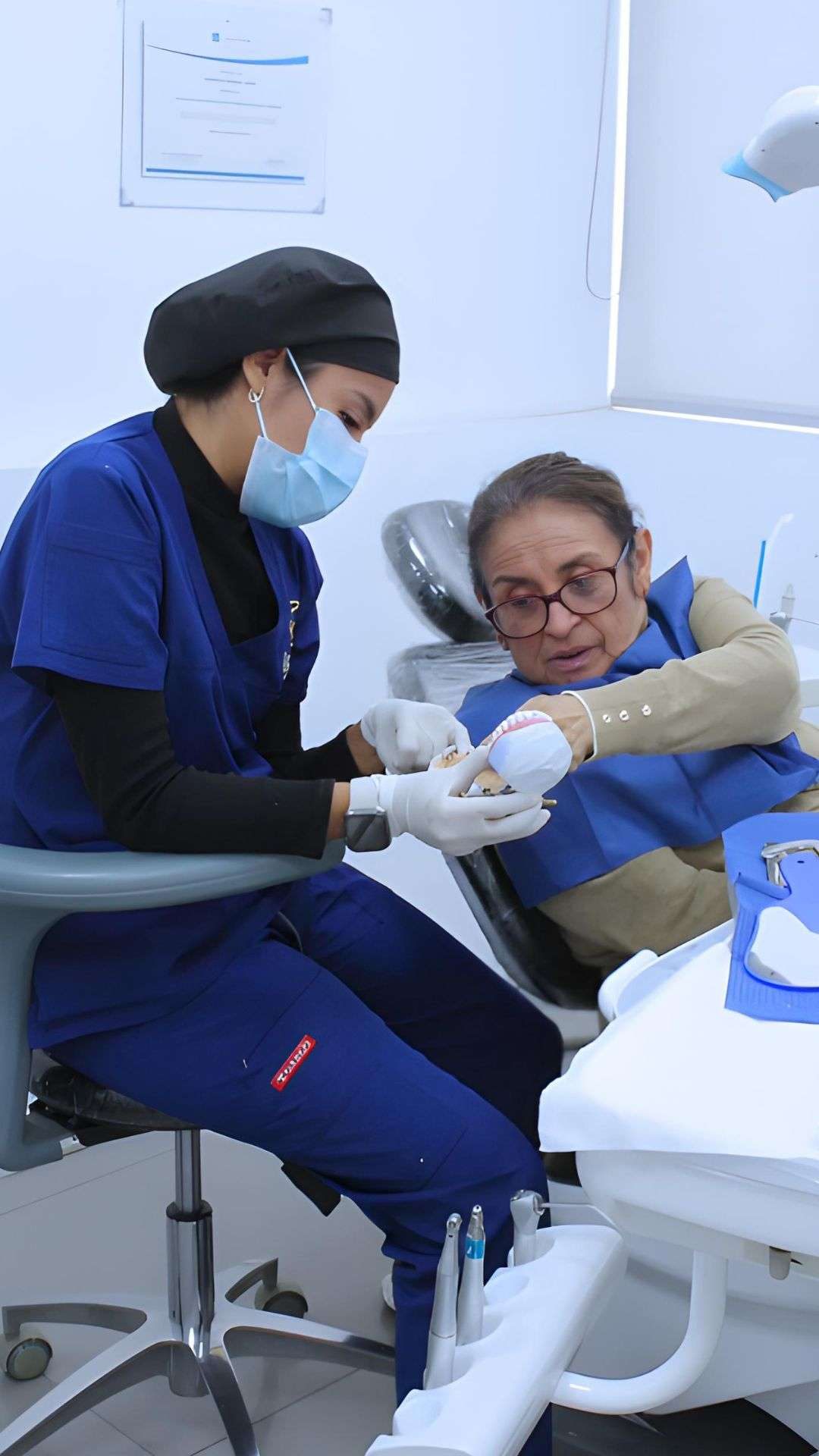 Odontóloga explicando un tratamiento con un modelo dental a una paciente mayor